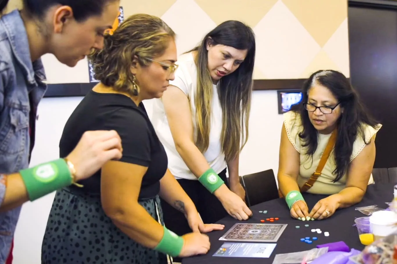 Four educators in green wristbands lean over a table, working a puzzle board together